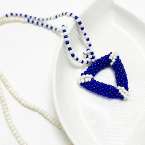 Azure Handmade Beaded Necklace featuring a 3D handwoven blue and white triangle pendant on a coordinating seed bead chain resting on a white decorative plate.