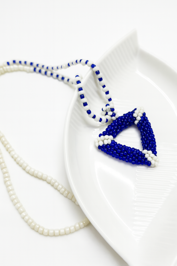 Azure Handmade Beaded Necklace featuring a 3D handwoven blue and white triangle pendant on a coordinating seed bead chain resting on a white decorative plate.