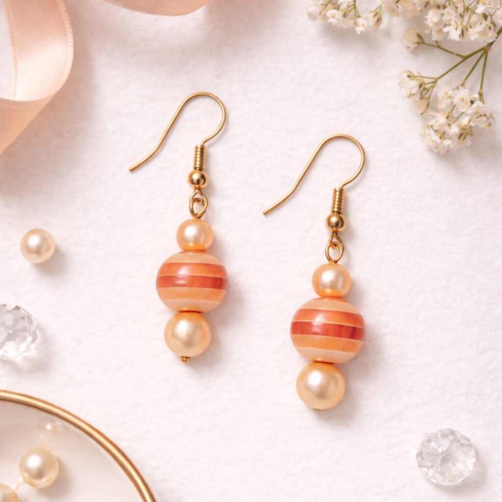 Sunset Glow Dangle Earrings featuring peach-and-white striped beads and cream pearls on gold fishhook wires displayed on a white textured background.