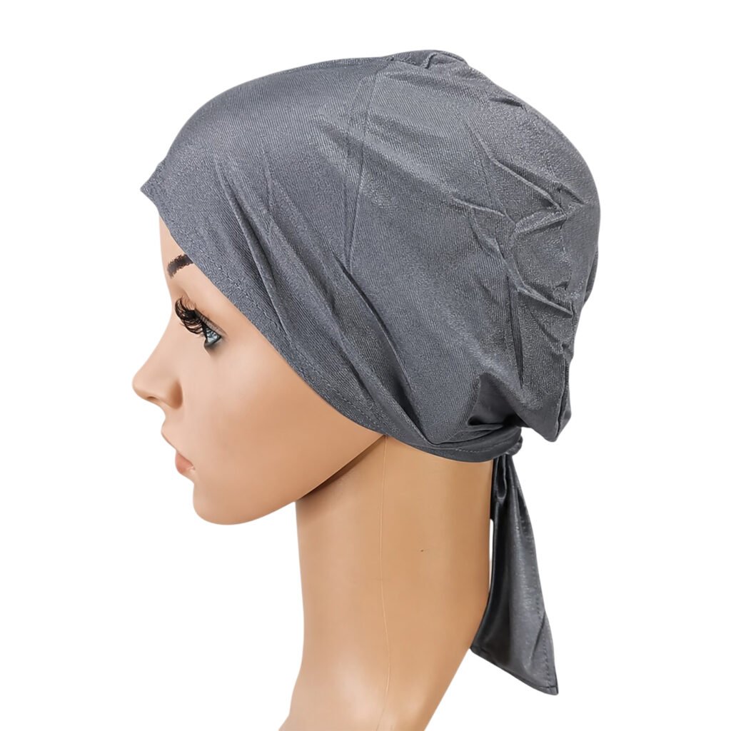 A side profile view of a mannequin wearing an adjustable Tie Back UnderScarf Cap, demonstrating the comfortable stretch fit and the fabric tie bands at the back.